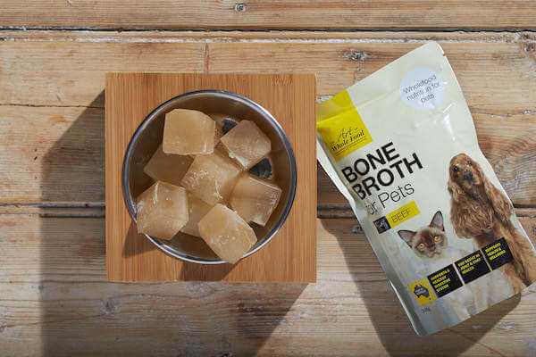 Bone Broth Beef pet food ice cubes in bowl with 500ml pouch on wooden surface