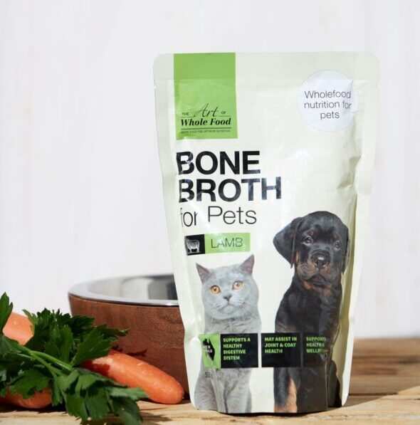 Bone Broth Lamb pet food pouch with dog and cat images on wooden table with carrot and parsley ingredients