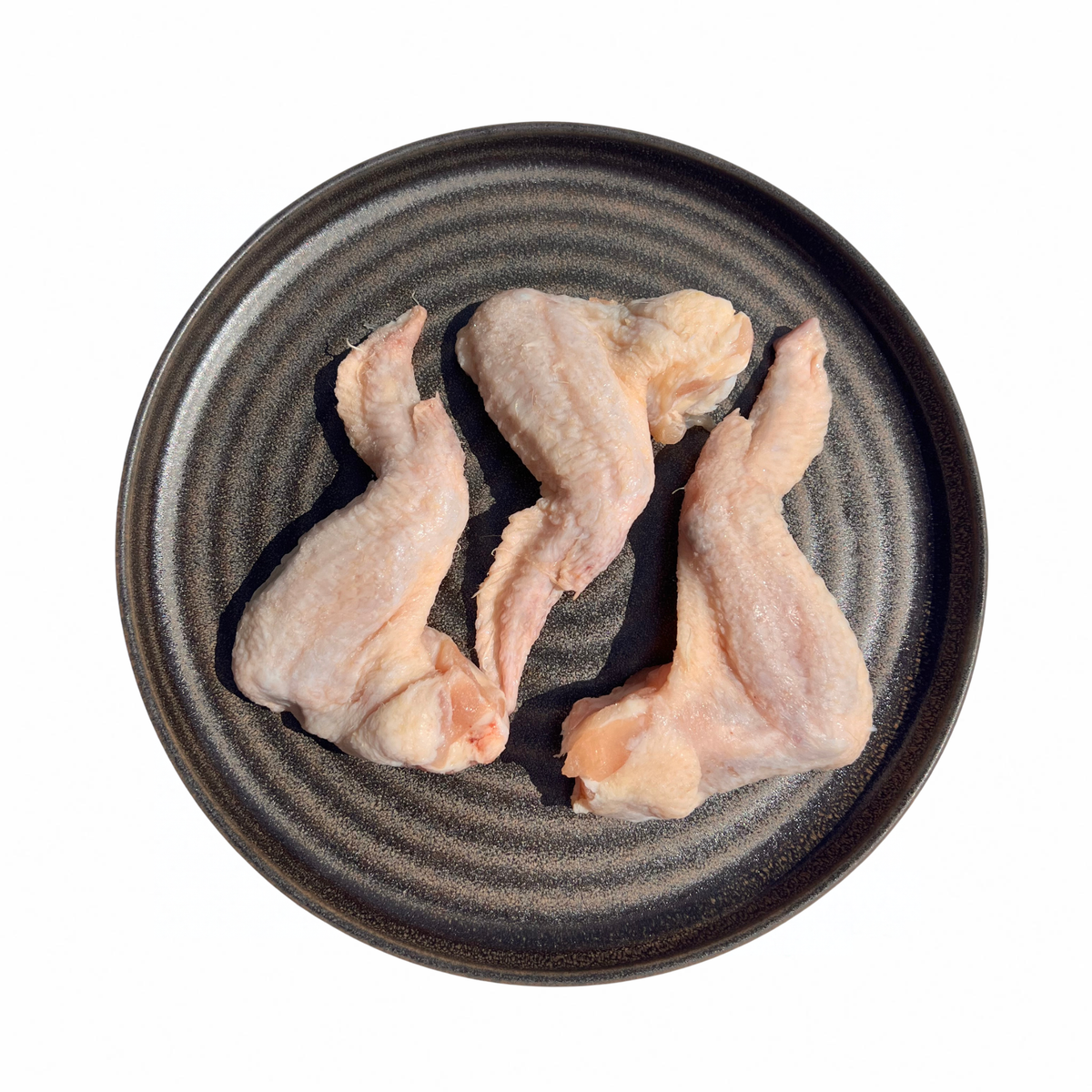 Three raw chicken wings arranged on a round dark gray ceramic plate with concentric rings, photographed from above on a white background.